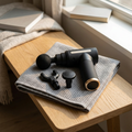 Percussion massage gun with spare attachment heads resting on a folded towel on an oak bench